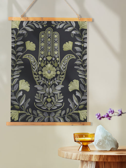 a Botanical Hamsa wall tapestry featuring intricate sage green and lavender design on black background, showing a protective hand symbol surrounded by leaf motifs and floral elements, hanging from wooden dowels with natural twine.painting of a hamsa hanging on a wall